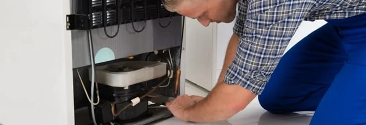 Refrigerator repair technician servicing the compressor and condenser area in Santa Ana, CA