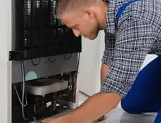 Refrigerator repair technician servicing the compressor and condenser area in Santa Ana, CA